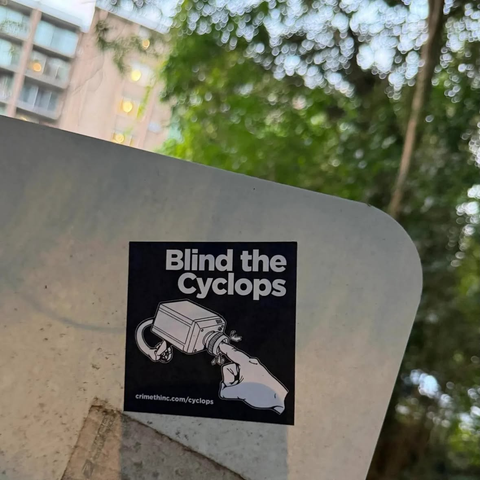 Adesivo b/n di Cr!meth!nc "Blind the Cyclops" con un dito conficcato dentro una telecamera di sorveglianza.